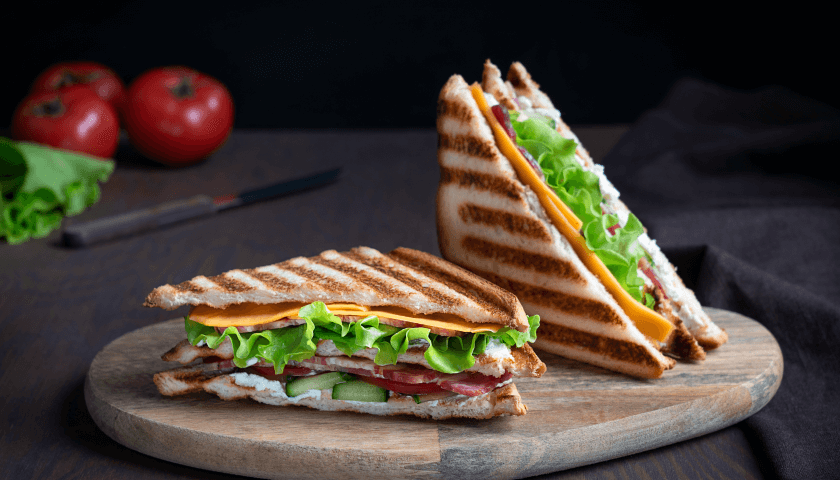 Two meat and cheese sandwiches with tomatoes between toasted bread