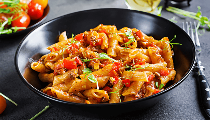 Penne pasta in meaty tomato sauce, adorned with tomatoes and pea sprouts